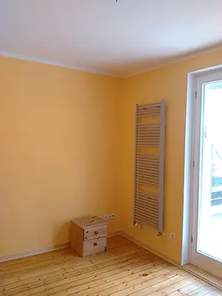 Orange gestrichenes Zimmer mit Heizkörper und Balkontür